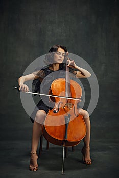 Cellist& x27;s debut, classical album. Elegant young woman making solo performance, playing cello against dark vintage