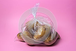 Cellophane bag with potatoes on a pink background.