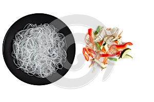 Cellophane or glass noodles in black matte plate and colorful chopped fresh vegetables mix isolated on a white background, top