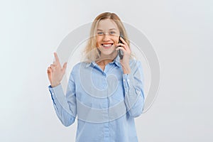 Cellphone, cellular concept. Smiling happy blonde woman talking on mobile phone, gestures with hand, pointing finger up, showing