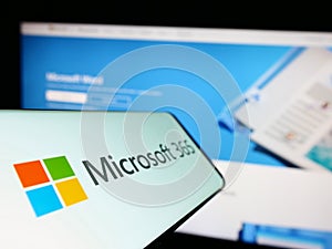 Cellphone with logo of productivity software Microsoft 365 on screen in front of company website.