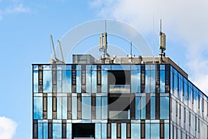 Cellular antennas on modern building roof. Surface reflects Clouds