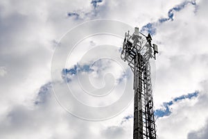 Cellular communications tower on cloudy sky background in daytime, copy space.