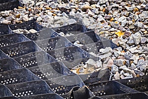 Cellular confinement system - plastic black honeycomb frame filled with small natural stones closeup. Used in construction for