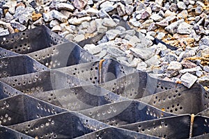 Cellular confinement system - plastic black honeycomb frame filled with small natural stones closeup. Used in construction for