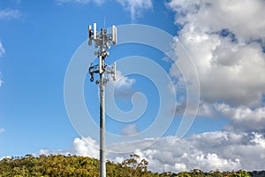 Cellular, mobile phone transmitter tower with blue sky and clouds left