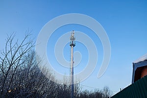 Cellular tower in village on winter sunny day or evening and blue sky background