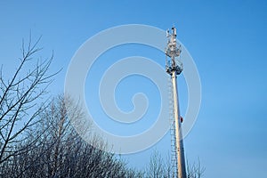 Cellular tower in village on winter sunny day or evening and blue sky background
