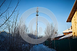 Cellular tower in village on winter sunny day or evening and blue sky background