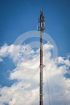 Cellular transmission tower with white clouds and blue sky background.