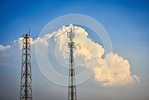 Cellular transmission towers with white clouds and blue sky background.