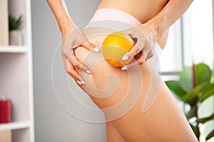 Cellulite problem, young woman holding orange near her leg