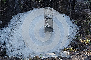 Cement and concrete has splashed up a black metal fence post during construction of a fence