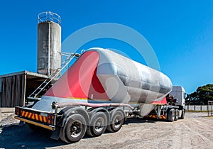 Cement delivery truck with multiple wheels and silo in background