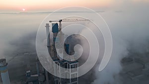 Cement factory with high concrete plant structure and tower crane at industrial manufacturing site on foggy evening