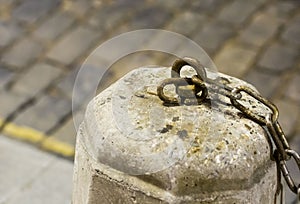 Cement gray pedestal with an iron hook and part of the chain windblown on a blurred background road