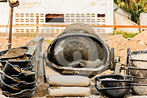 Cement mixer machine is at construction site with two wheelbarrows tools sand and cement bag.