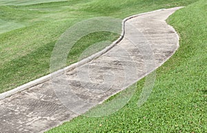 Cement path curving through green lawn in golf course.