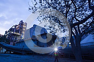 Cement plant factory manufacturing at dusk, sparks of worker with headlamp flashlight during working overtime