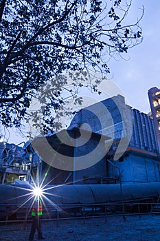 Cement plant factory manufacturing at dusk, sparks of worker with headlamp flashlight during working overtime