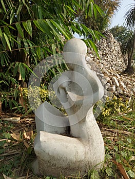 A cement sculpture of a breastfeeding of mother hideing her child near a bush