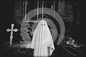 In the of a cemetery, next to a crypt, stands a ghost in a black-white photo, evoking a feeling of mystery and horror. Halloween