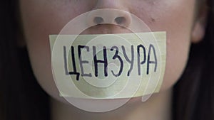 Censorship word in Russian on tape, woman removing mouth sticker, restriction