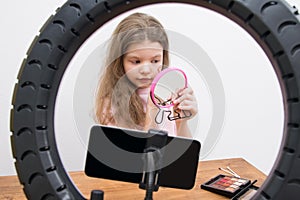 In the center of a circular lamp and a smartphone, a blogger girl makes a make-up, draws a heart on her cheek