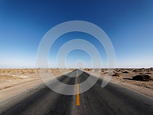 Centered view of an endless asphalt road in desert, low angle straight rough road with blue sky background, magic world