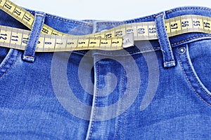 Centimeter tape as belt in jeans close-up, concept of losing weight. Healthy lifestyle.