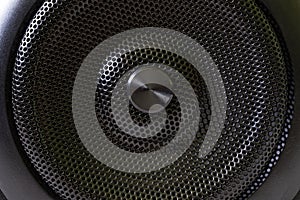 The central fragment of a modern audio speaker with a protective black metal grille. Macro