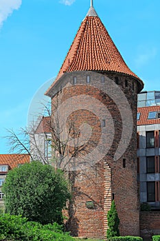 Centuries old red brick tower with cone shaped red tile roof in city setting