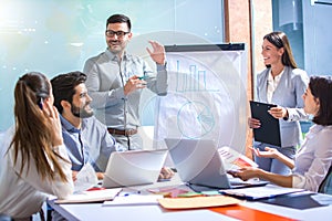 CEO business leader with hands gesture explaining profit oscillations to his colleagues on flip chart at conference room