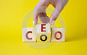 CEO and COO symbol. Businessman hand turns wooden cubes and changes word CEO to COO. Beautiful yellow background. CEO and COO and
