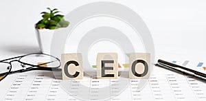 CEO word concept written on wooden blocks, cubes on a light table with flower ,pen and glasses on chart background