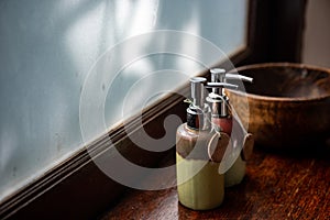 Ceramic bottles of shampoo and shower gel are placed in a large wooden bowl. And put on the wooden counter