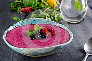 Ceramic bowl with berry smoothie decorated with currant, raspberry and mint on the black wooden background - Well being, Healthy e