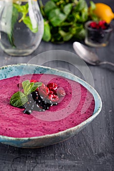 Ceramic bowl with berry smoothie decorated with currant, raspberry and mint on the black wooden background - Well being, Healthy e