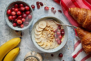 Ceramic bowl of oatmeal porridge with banana, fresh cranberries and walnuts