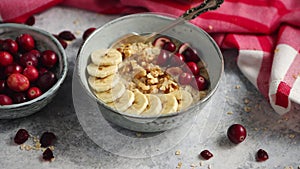 Ceramic bowl of oatmeal porridge with banana, fresh cranberries and walnuts