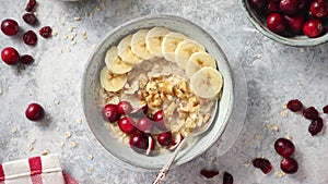 Ceramic bowl of oatmeal porridge with banana, fresh cranberries and walnuts