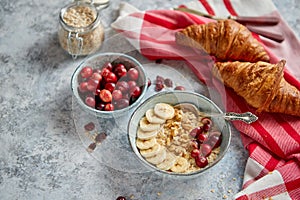 Ceramic bowl of oatmeal porridge with banana, fresh cranberries and walnuts