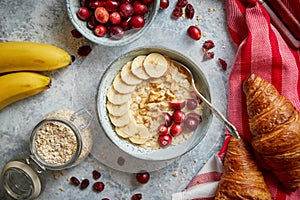 Ceramic bowl of oatmeal porridge with banana, fresh cranberries and walnuts