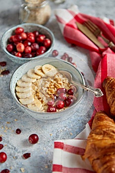 Ceramic bowl of oatmeal porridge with banana, fresh cranberries and walnuts