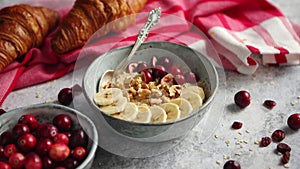 Ceramic bowl of oatmeal porridge with banana, fresh cranberries and walnuts