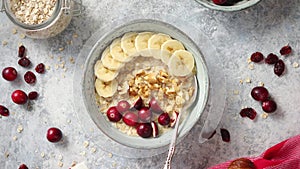 Ceramic bowl of oatmeal porridge with banana, fresh cranberries and walnuts