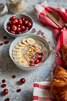 Ceramic bowl of oatmeal porridge with banana, fresh cranberries and walnuts