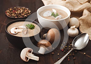 Ceramic bowl plates of creamy chestnut champignon mushroom soup with spoon, pepper and kitchen cloth on dark wooden  background