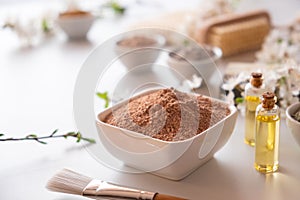 Ceramic bowl with red clay powder, ingredients for homemade facial and body mask or scrub and fresh sprig of flowering cherry