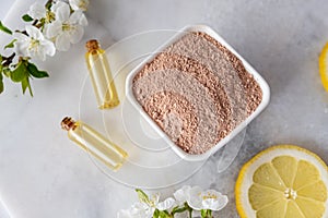 Ceramic bowl with red clay powder, ingredients for homemade facial and body mask or scrub and fresh sprig of flowering cherry